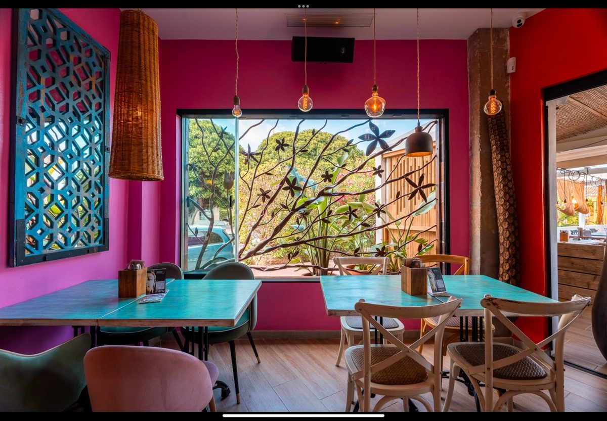 Comedor rosa con mesas turquesa junto al ventanal